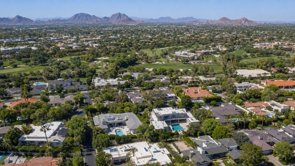 Aerial view of upscale suburban neighborhood with pools, golf course fairways and distant mountains under clear blue sky