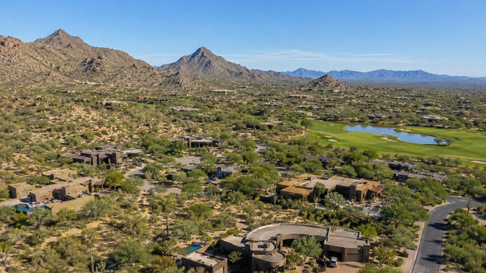 Aerial view of luxury desert homes, golf course and mountains with lake in Sonoran-style residential community