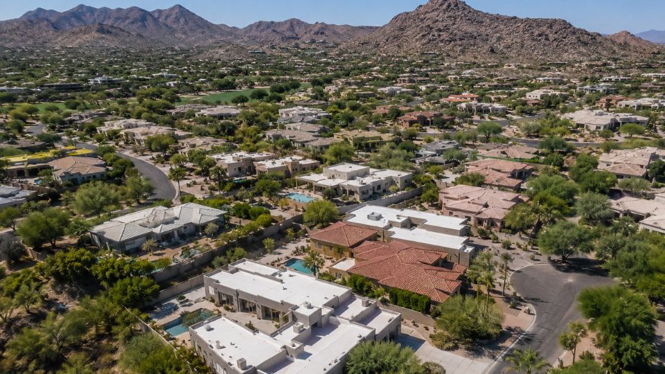 Aerial view of desert suburb with upscale tile-roof homes, backyard pools and rocky mountain backdrop