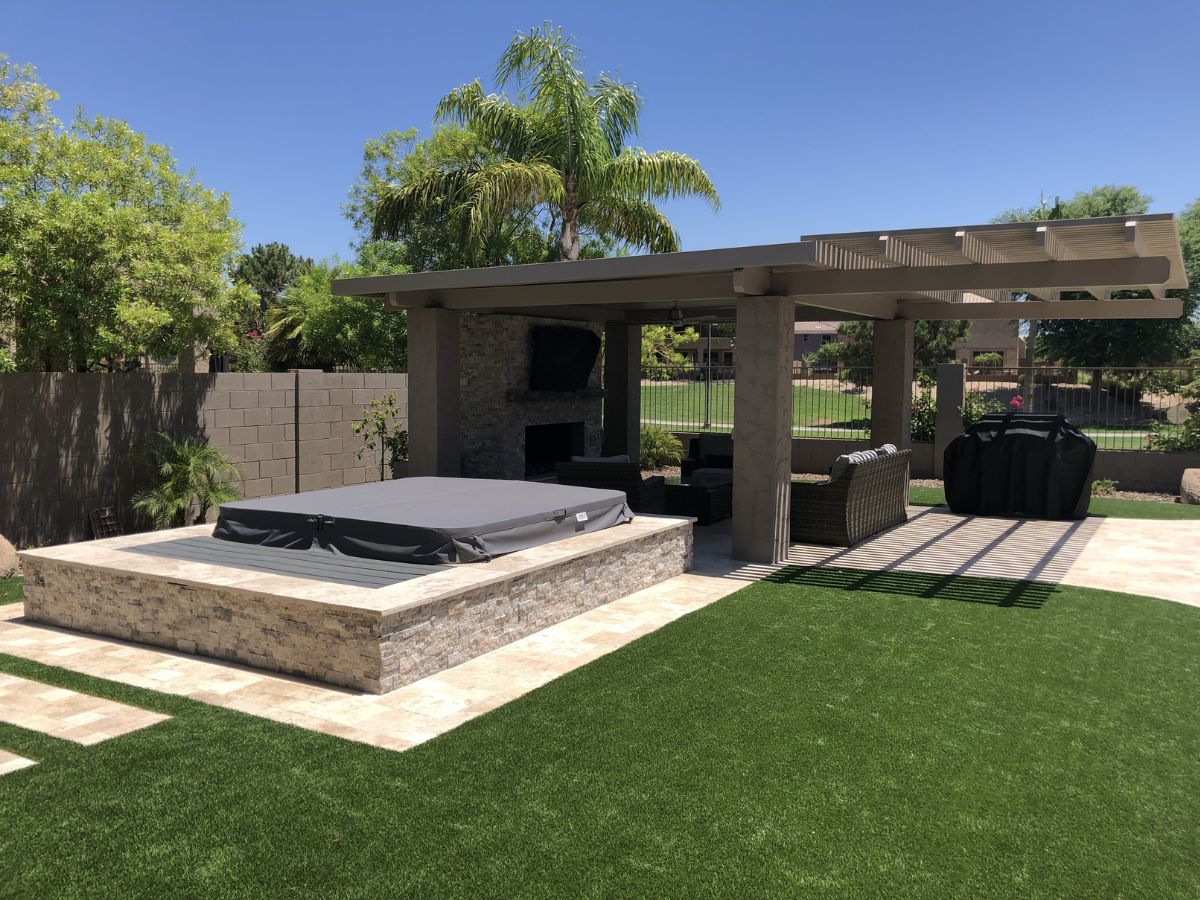 Backyard with covered pergola, stone hot tub surround, outdoor fireplace, lounge seating and BBQ on artificial turf