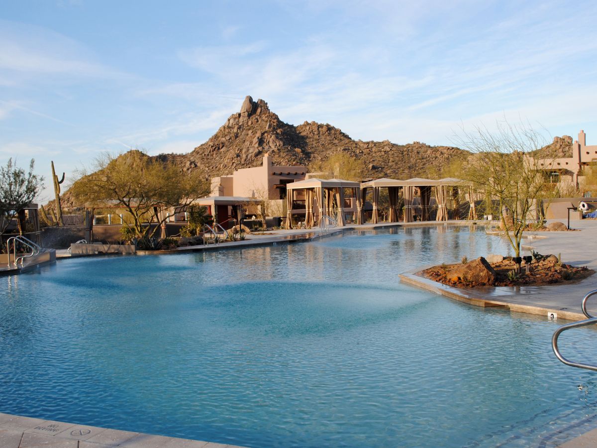 Luxury desert resort pool with blue water, private cabanas and rugged mountain backdrop under clear sky