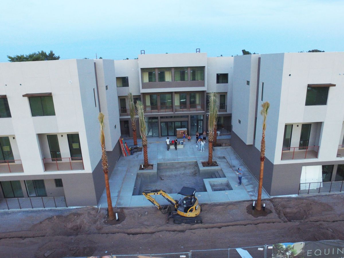 Aerial view of apartment complex courtyard under construction with mini excavator, palm trees and workers at new development