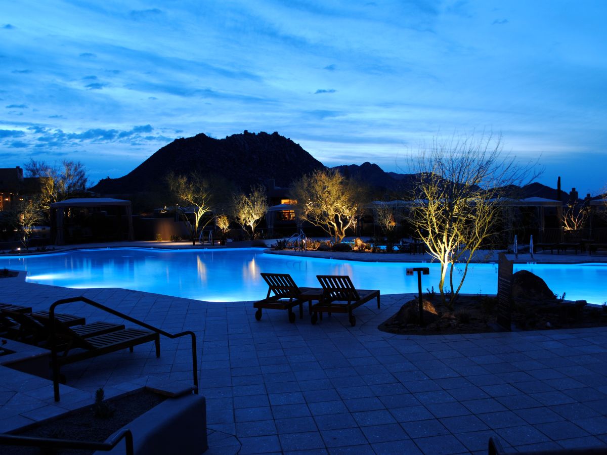 Resort pool at dusk with blue LED lighting, illuminated desert trees and mountain silhouette