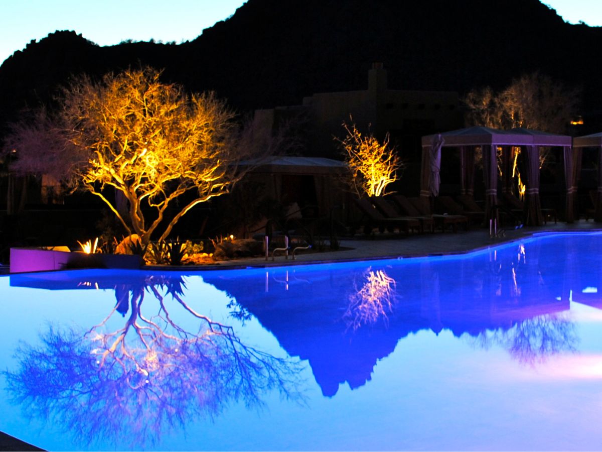 Night poolside scene with illuminated trees reflecting in vibrant blue swimming pool at luxury desert resort