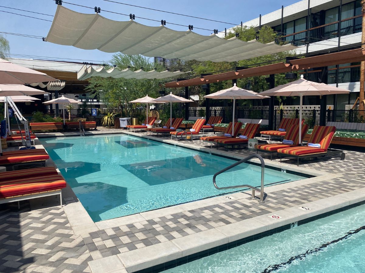 Luxury boutique hotel pool with striped sun loungers, umbrellas and overhead shade sails
