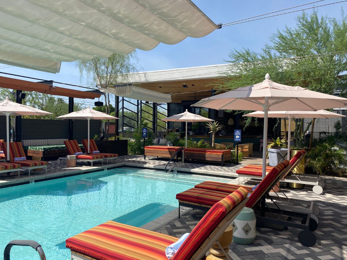 Resort outdoor pool with striped lounge chairs, beige umbrellas, shade canopy and poolside bar