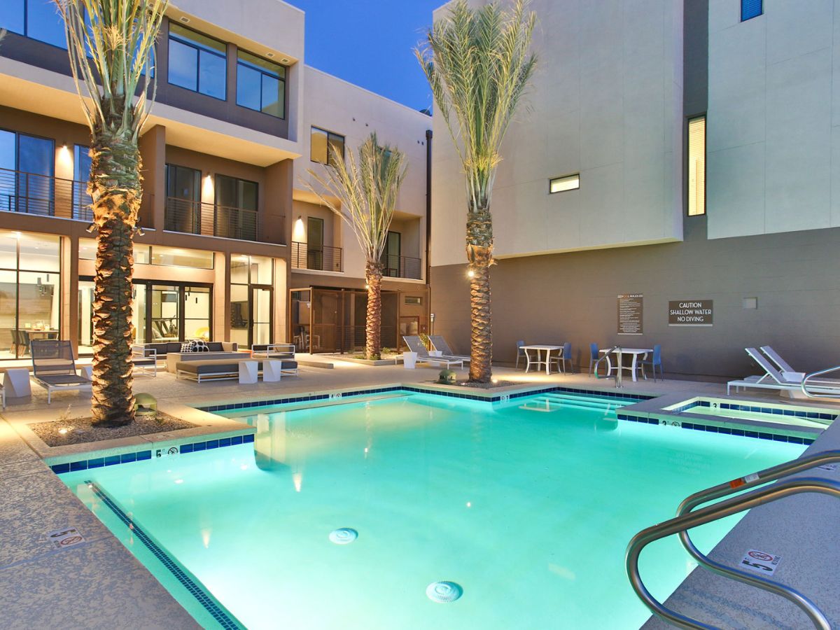 Luxury modern apartment courtyard pool with illuminated turquoise water, palm trees and lounge seating at dusk