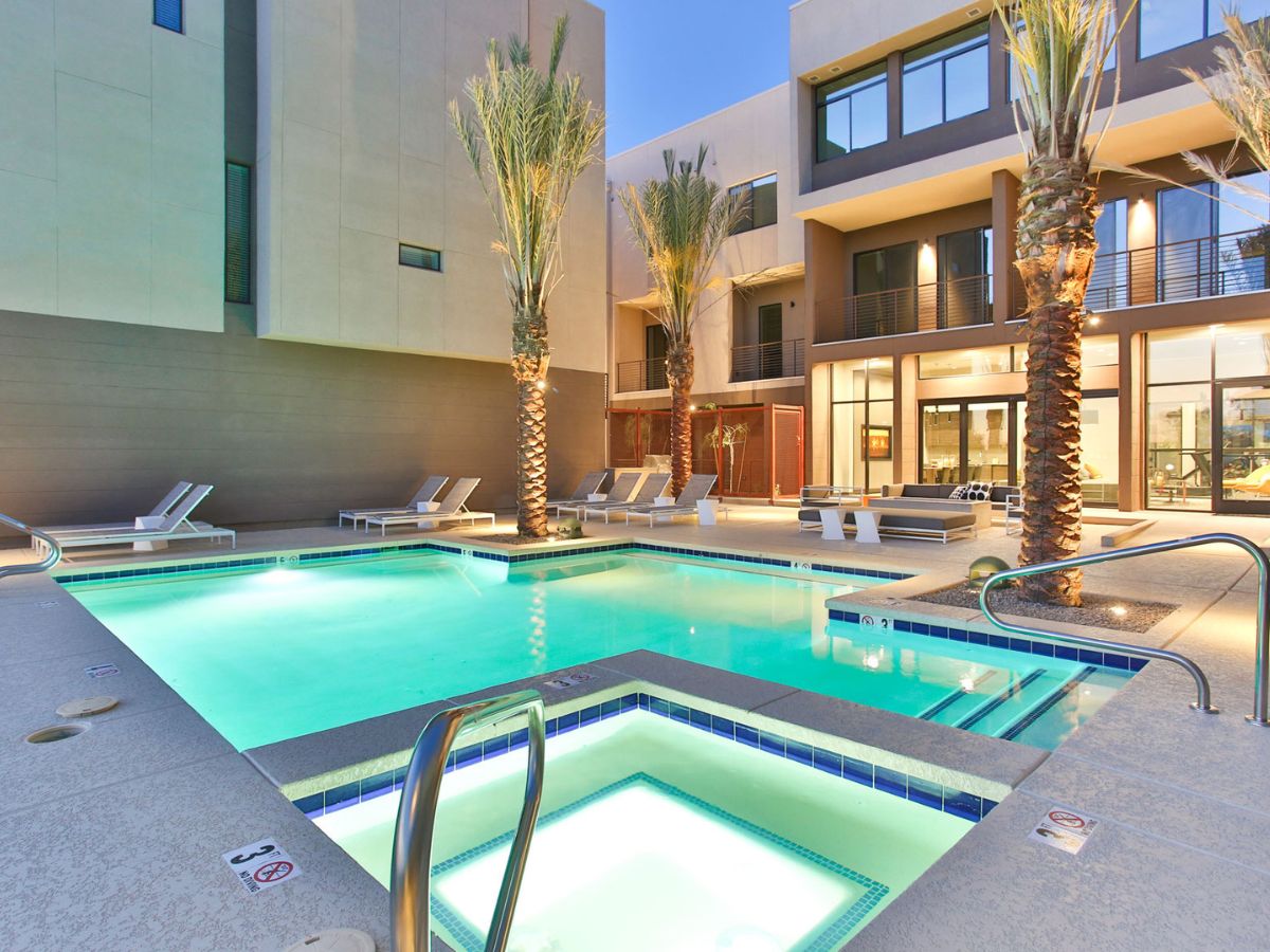 Modern apartment courtyard with illuminated swimming pool and spa, palm trees and lounge seating