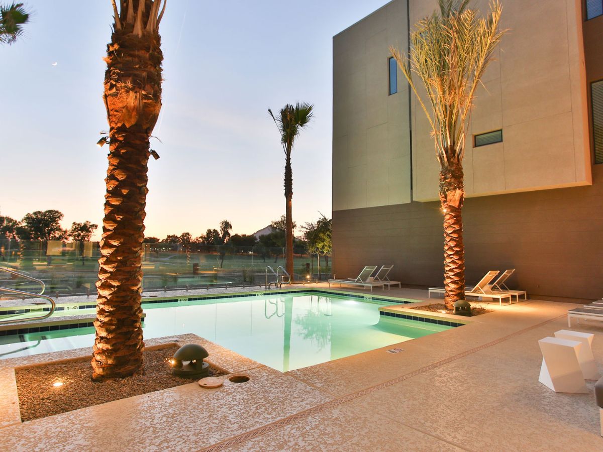 Hotel pool at sunset with illuminated palm trees, loungers, modern patio and glass fence