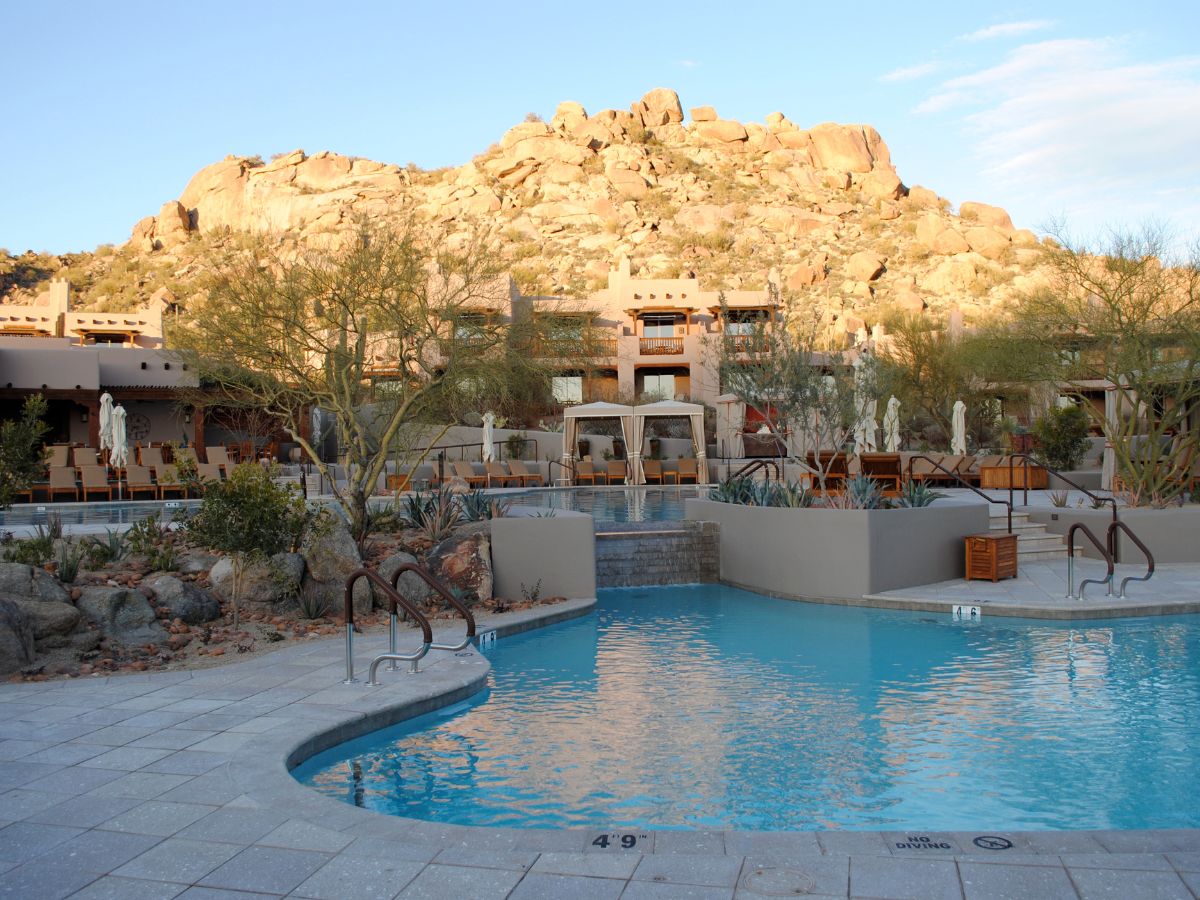 Desert resort pool with cabanas and rocky hill backdrop in warm evening light