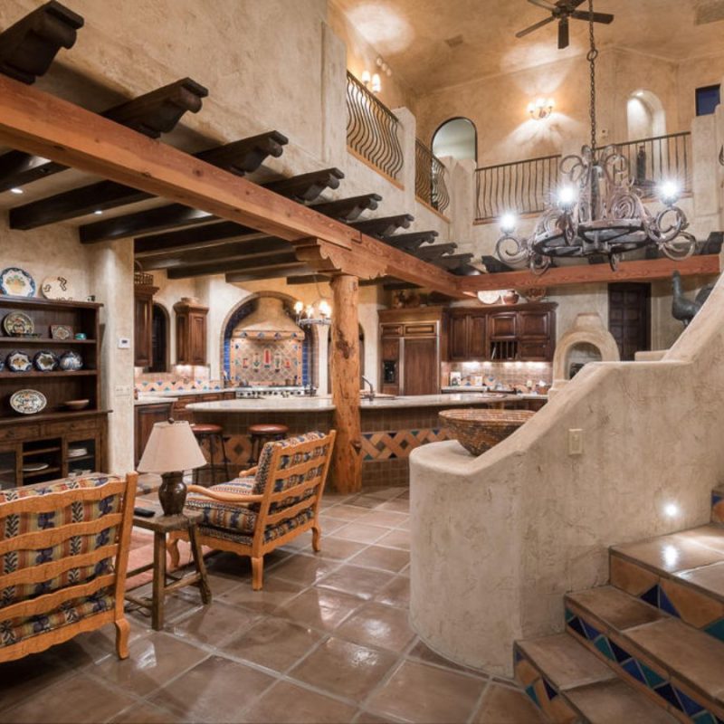 Southwestern open-concept living room and kitchen with exposed wooden beams, tiled staircase and wrought-iron chandelier