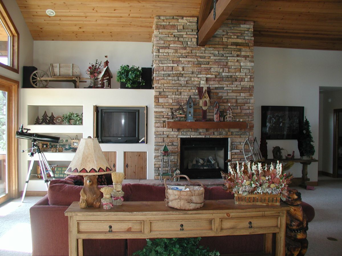 Rustic living room interior with stone fireplace, wooden vaulted ceiling, TV, telescope and console table with flowers