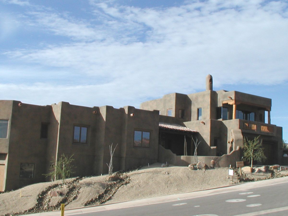 Two-story Southwestern adobe-style home with desert landscaping and stucco exterior under blue sky