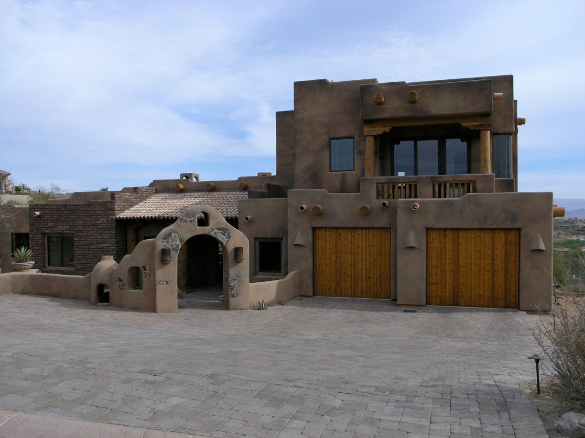 Southwestern adobe-style luxury home with wooden double garage doors, arched entryway and tiled roof