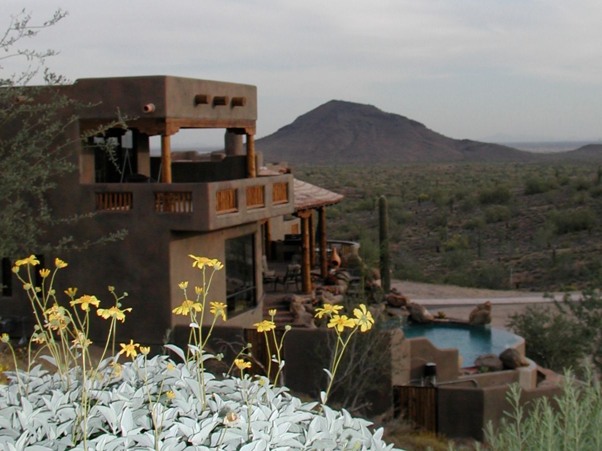 Adobe desert home with infinity pool, yellow wildflowers in foreground and sweeping mountain view