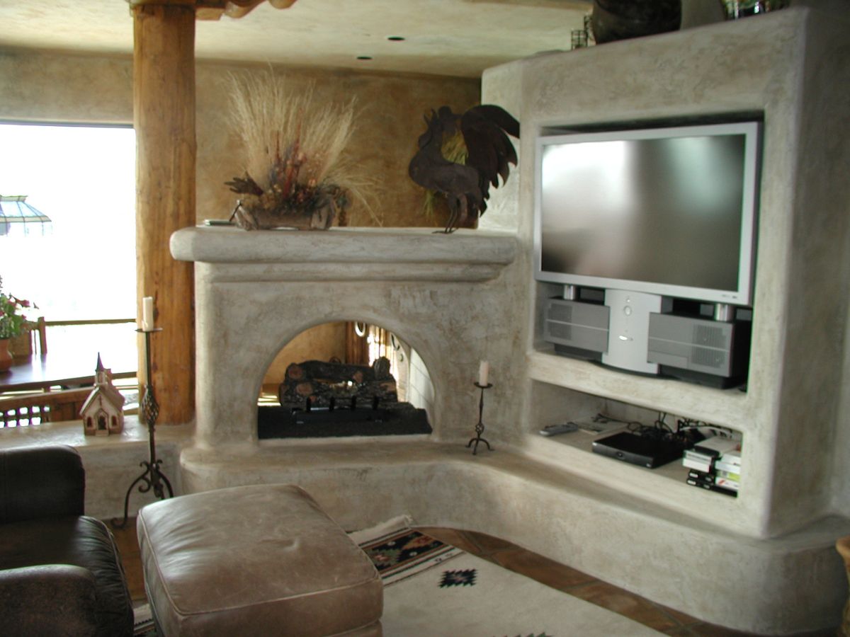 Southwestern living room with kiva-style plaster fireplace, built-in entertainment center with flat-screen TV and ottoman.