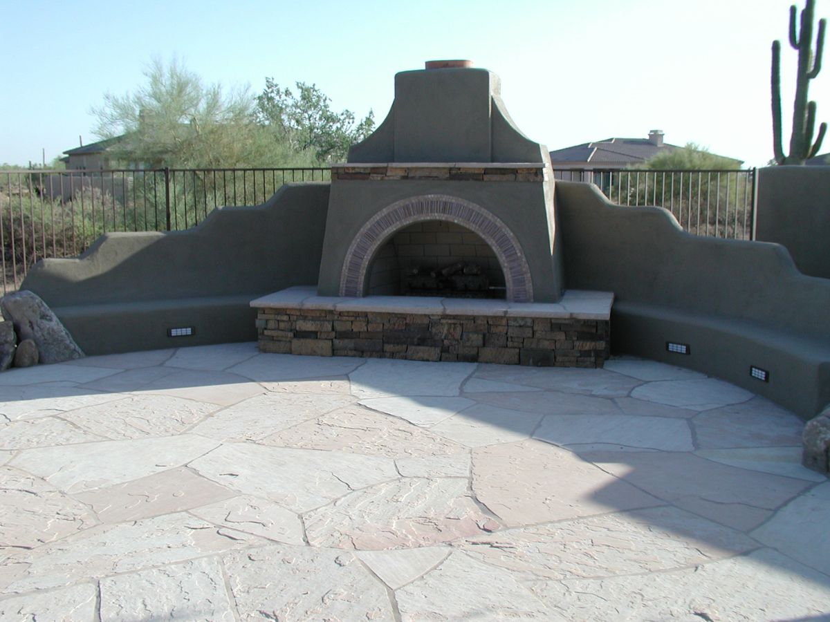 Adobe-style outdoor fireplace with curved built-in bench seating on light flagstone patio in desert yard