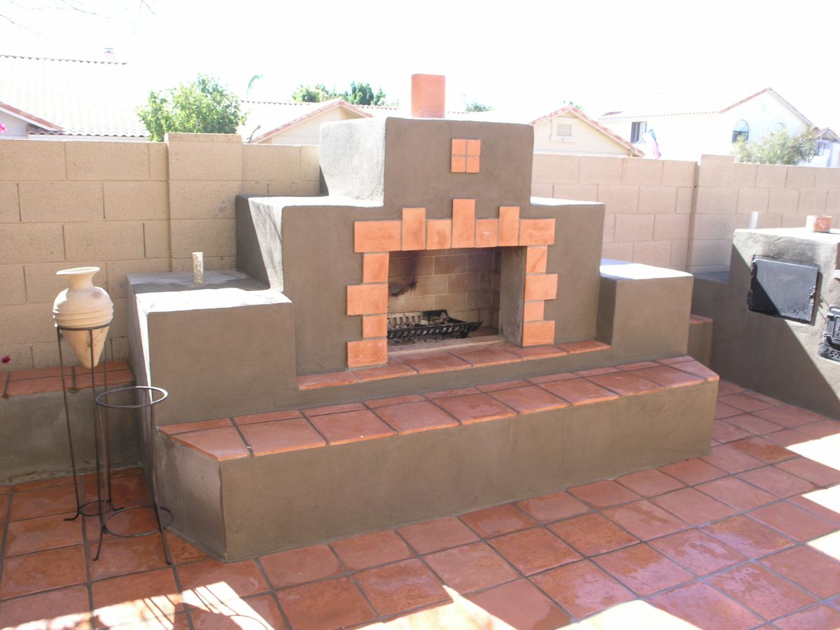 Southwestern-style outdoor stucco fireplace with terracotta tile seating and patio floor in backyard