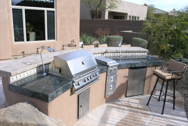 Outdoor backyard kitchen with stainless steel built-in grill, granite countertops, mini fridge and bar stool