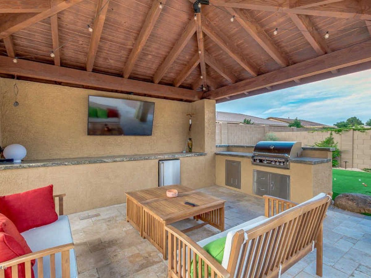 Outdoor kitchen and covered patio with wooden pavilion, built-in grill, wall TV and seating area
