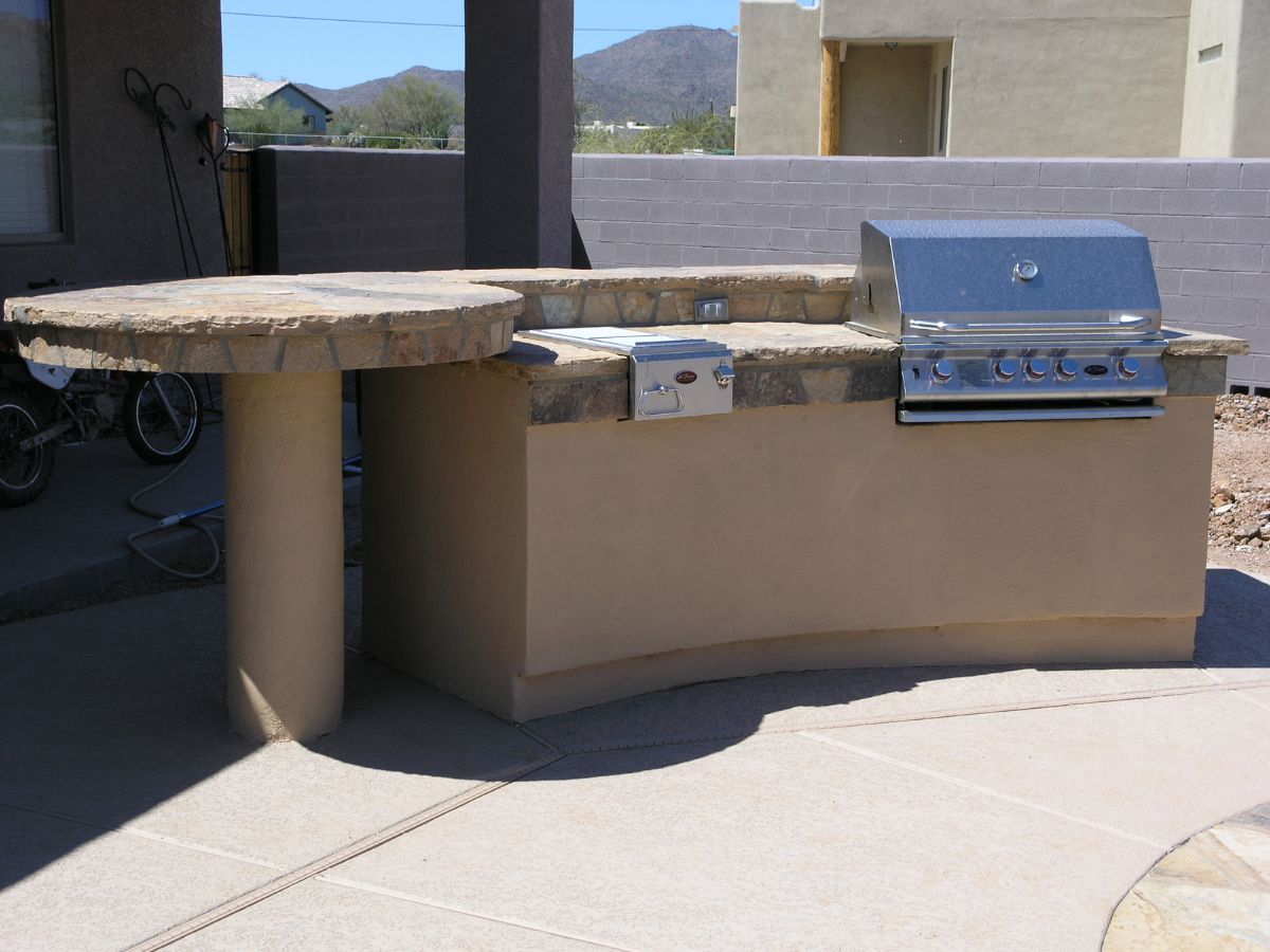 Outdoor kitchen island with built-in stainless steel gas grill and round stone countertop on patio
