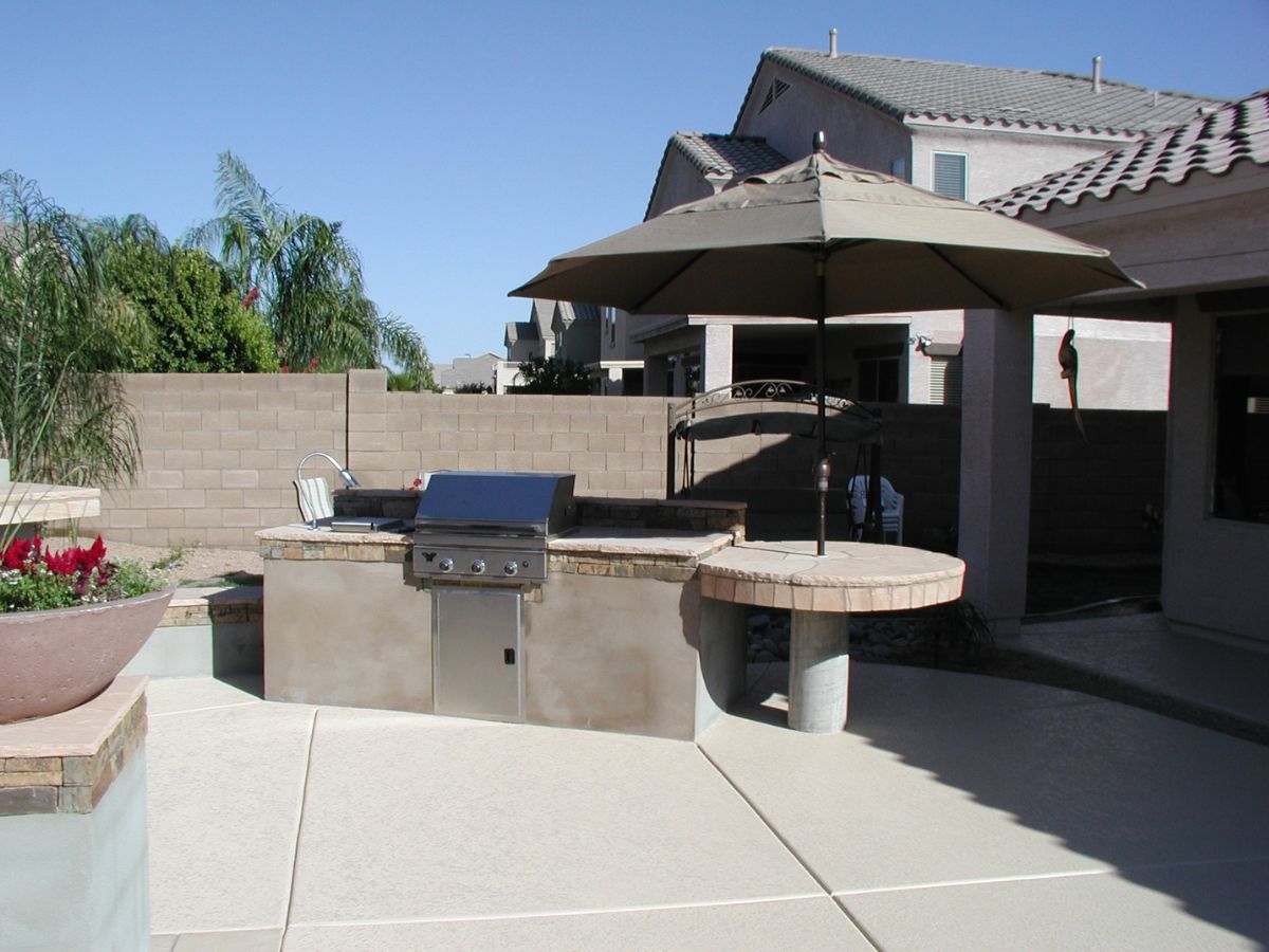 Backyard patio with built-in stainless gas grill, outdoor kitchen bar and umbrella-shaded round counter.