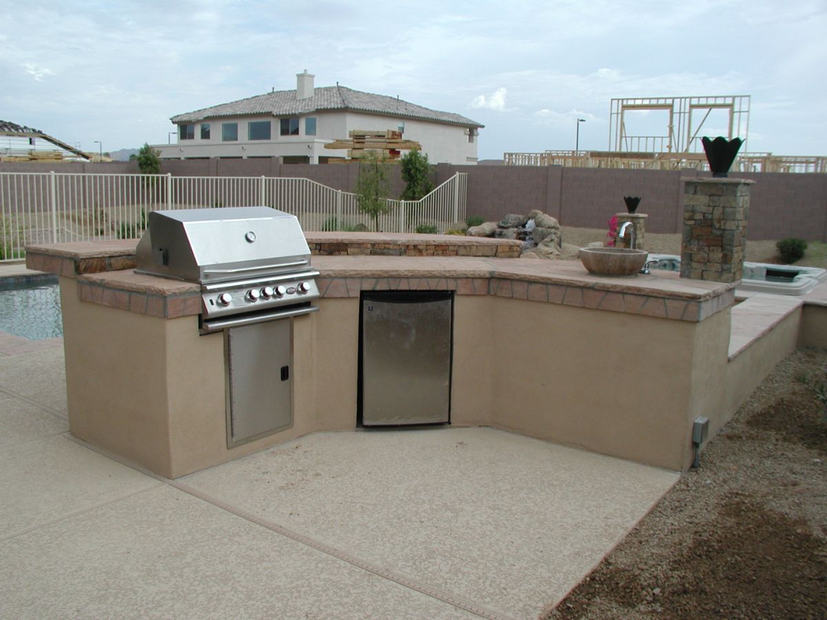 Poolside backyard outdoor kitchen with stainless steel built-in grill, mini fridge, sink and stone countertop