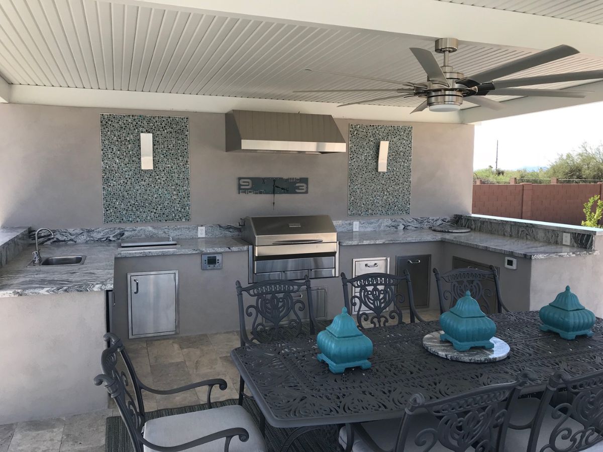 Outdoor covered kitchen patio with stainless grill, granite countertops, mosaic tile accents, ceiling fan and dining table.