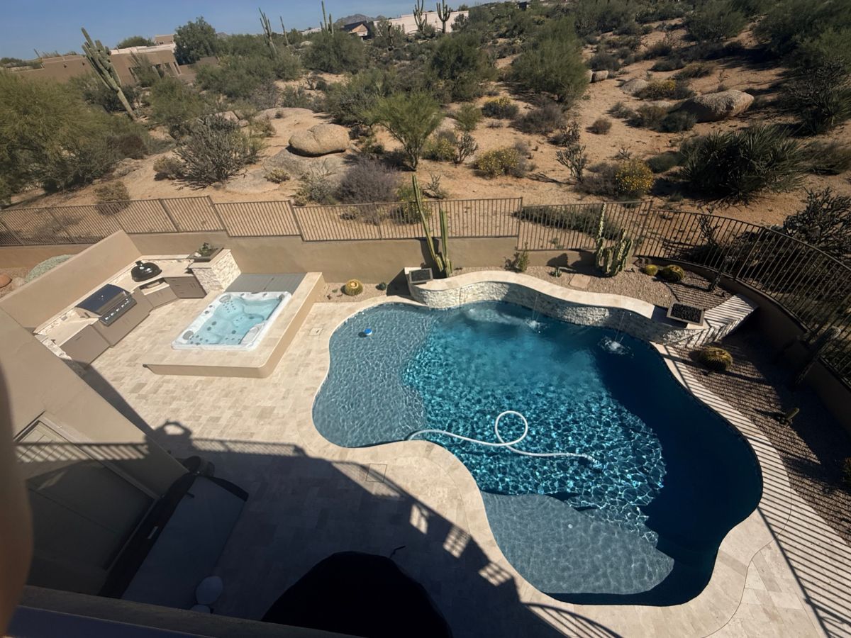 Aerial view of a luxury backyard pool and spa with outdoor kitchen, stone patio and desert landscape of cacti.