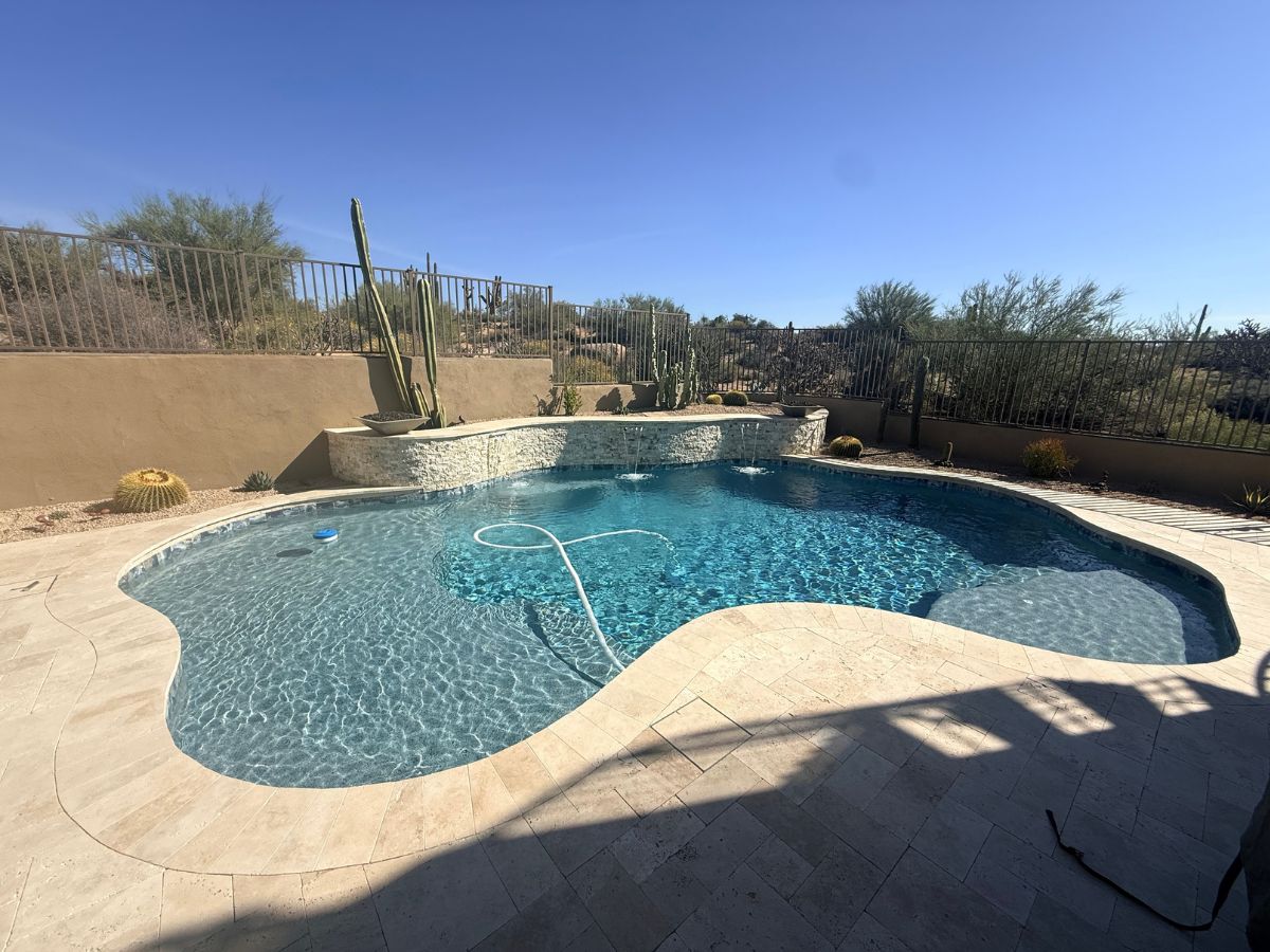 Backyard freeform swimming pool with clear blue water, travertine deck and desert landscaping with cacti
