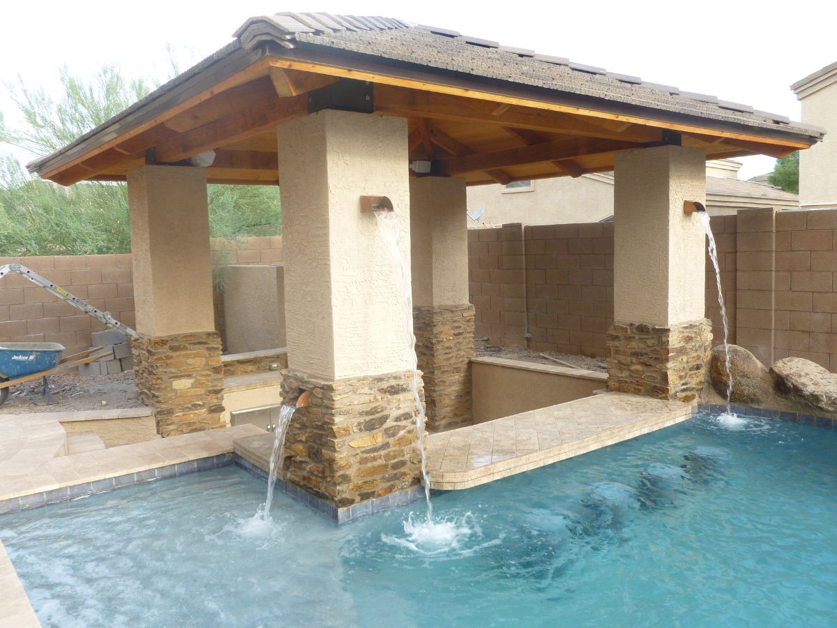 Backyard pool with pavilion cabana, stone-clad columns and three cascading water spouts over tiled swim-up ledge
