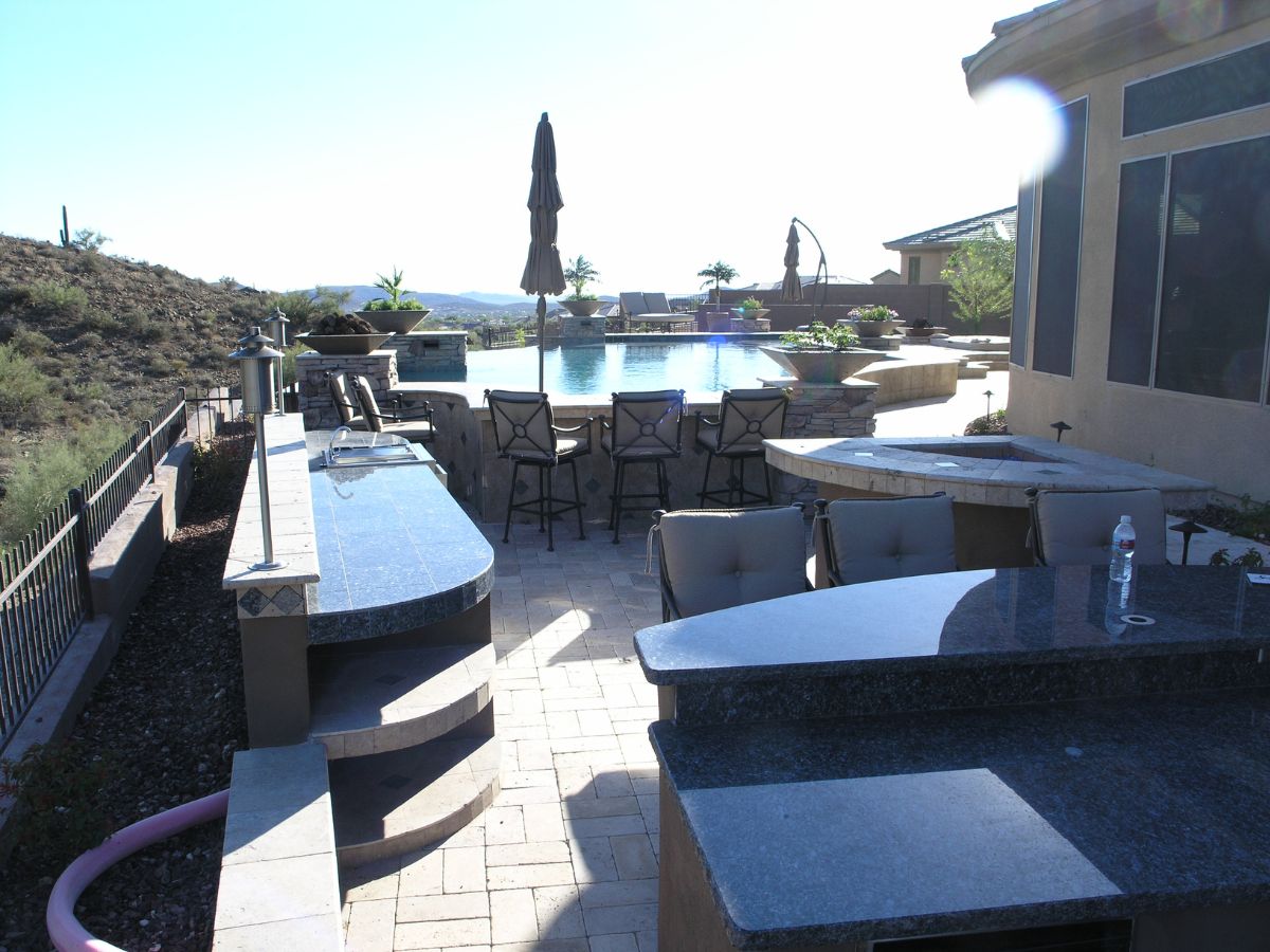 Luxury backyard pool and patio with granite bar counters, barstools, lounge chairs and desert hillside view
