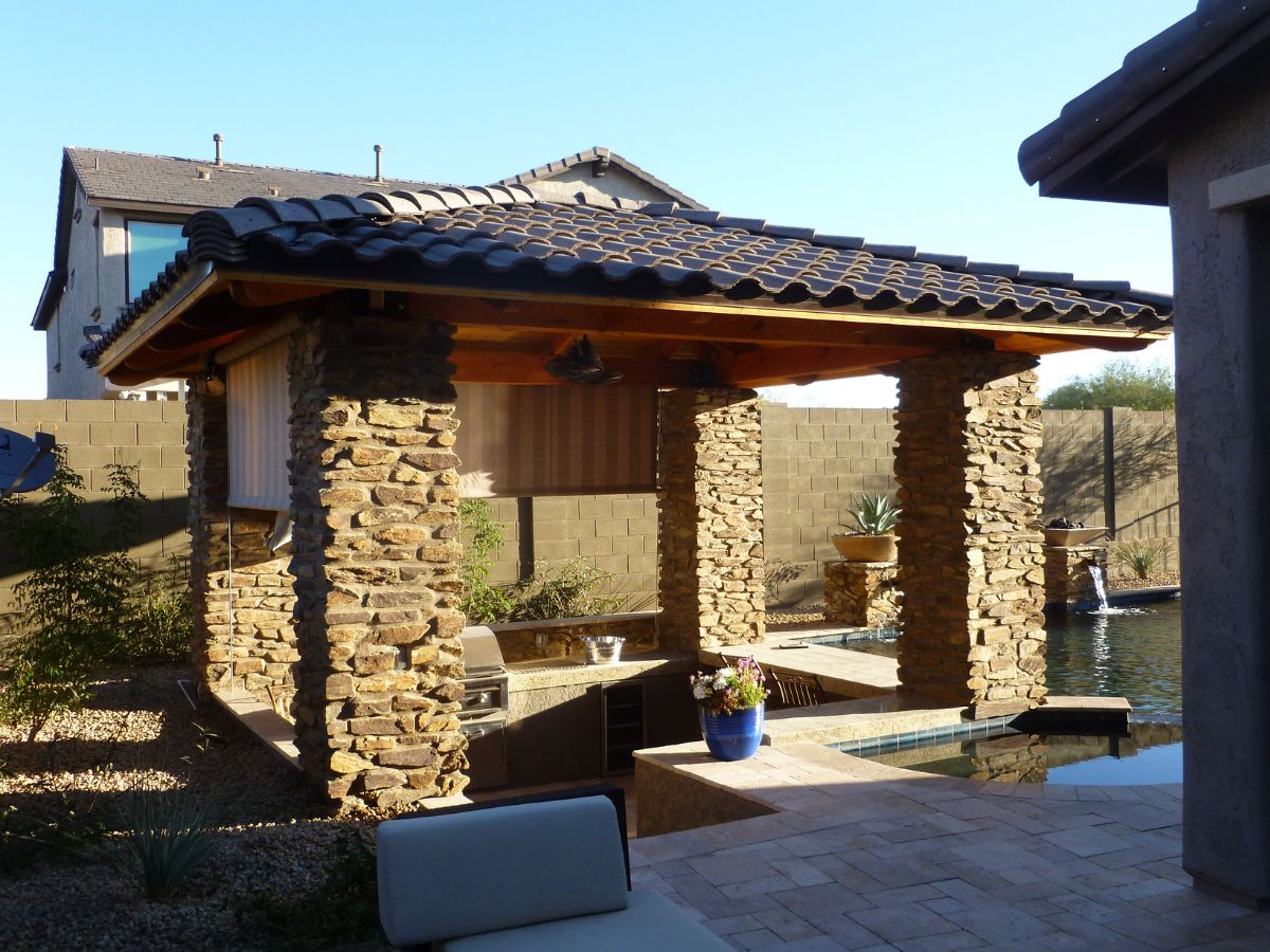 Backyard covered patio with stone pillars, tiled roof, outdoor kitchen and poolside seating