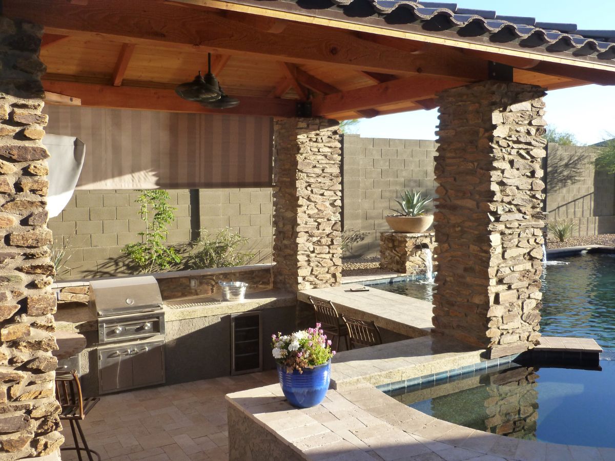 Backyard covered patio with outdoor kitchen, stone pillars, built-in grill, bar seating and swimming pool