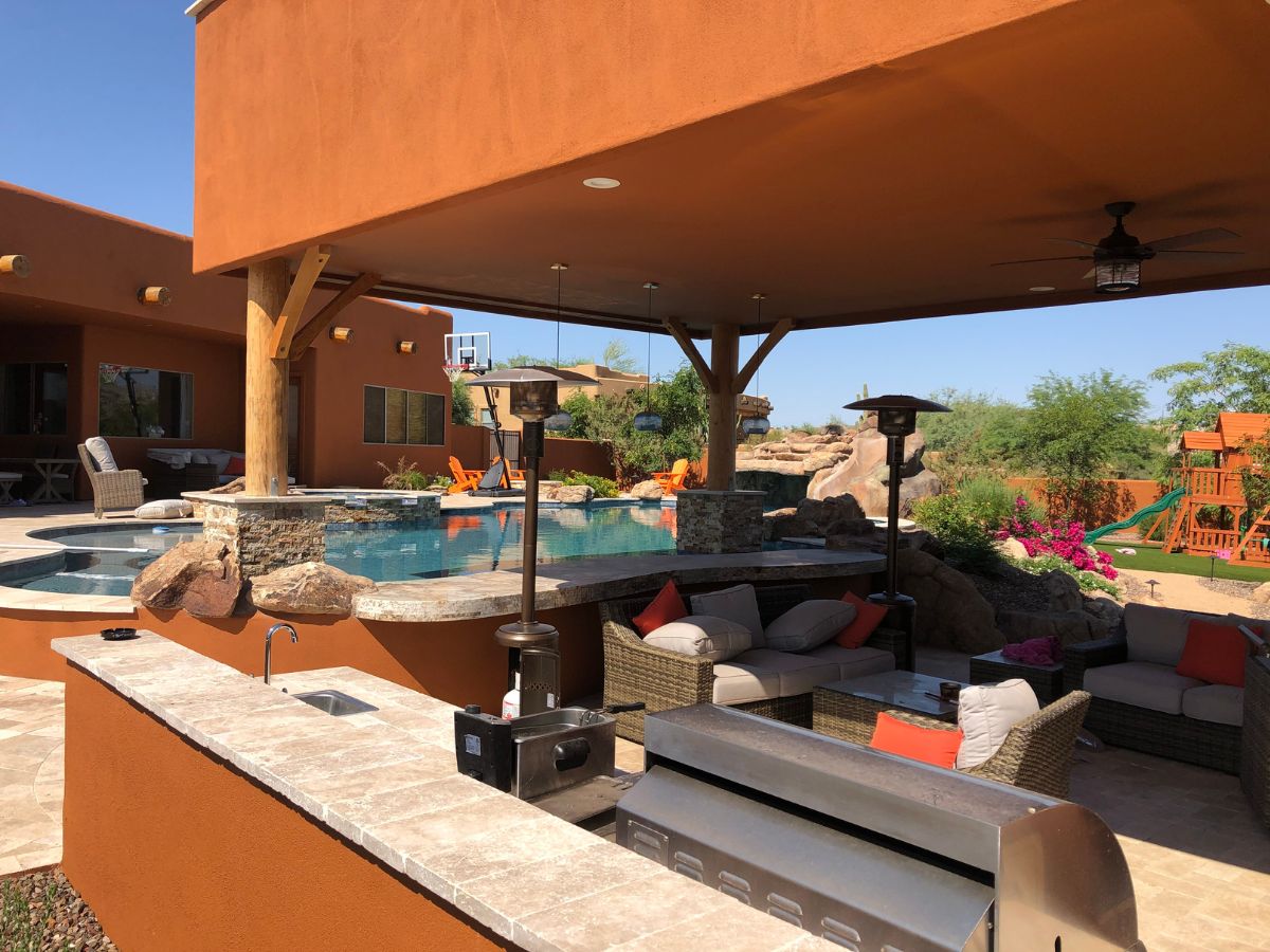 Luxury backyard oasis with covered patio, outdoor kitchen, wicker seating and pool with rock waterfall