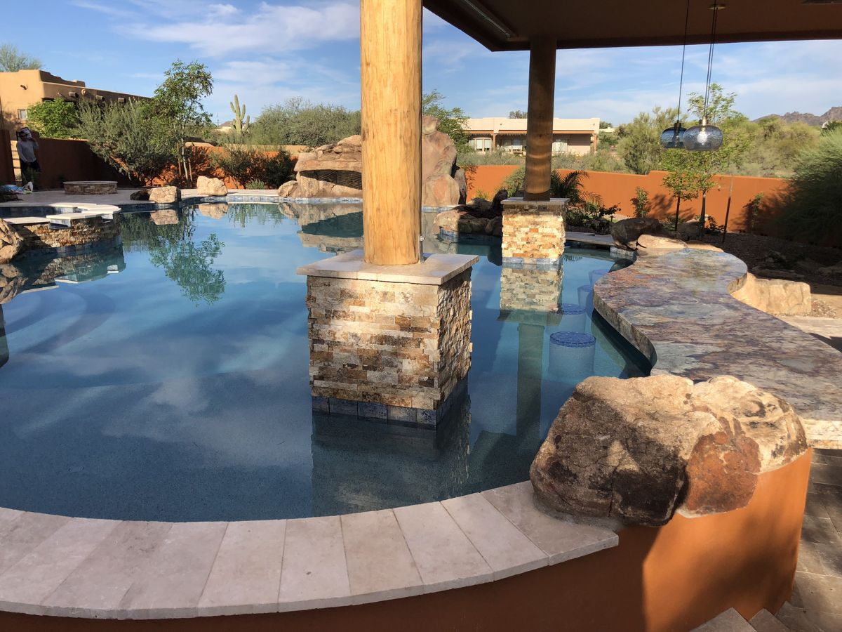 Resort-style backyard pool with stone-clad columns, swim-up bar, rock waterfall and desert landscaping