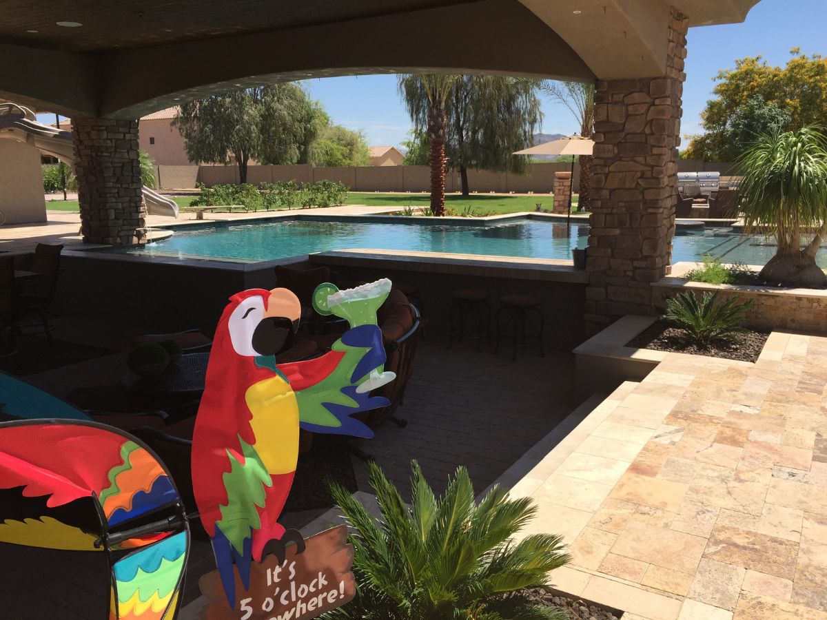 Backyard pool patio with tiled deck, palm trees and colorful parrot cocktail sign reading It's 5 o'clock somewhere
