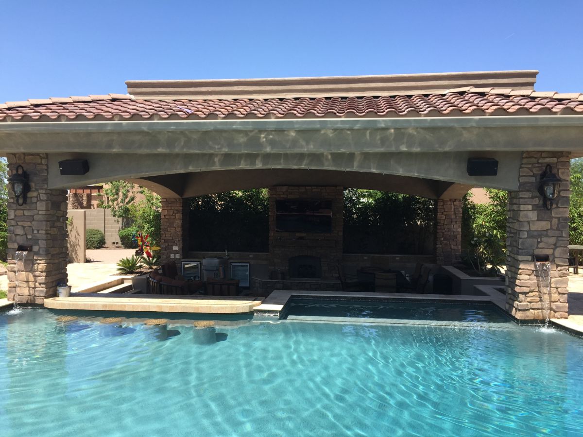 Backyard pool with swim-up bar, covered patio and outdoor kitchen under tiled roof, stone columns and water features.