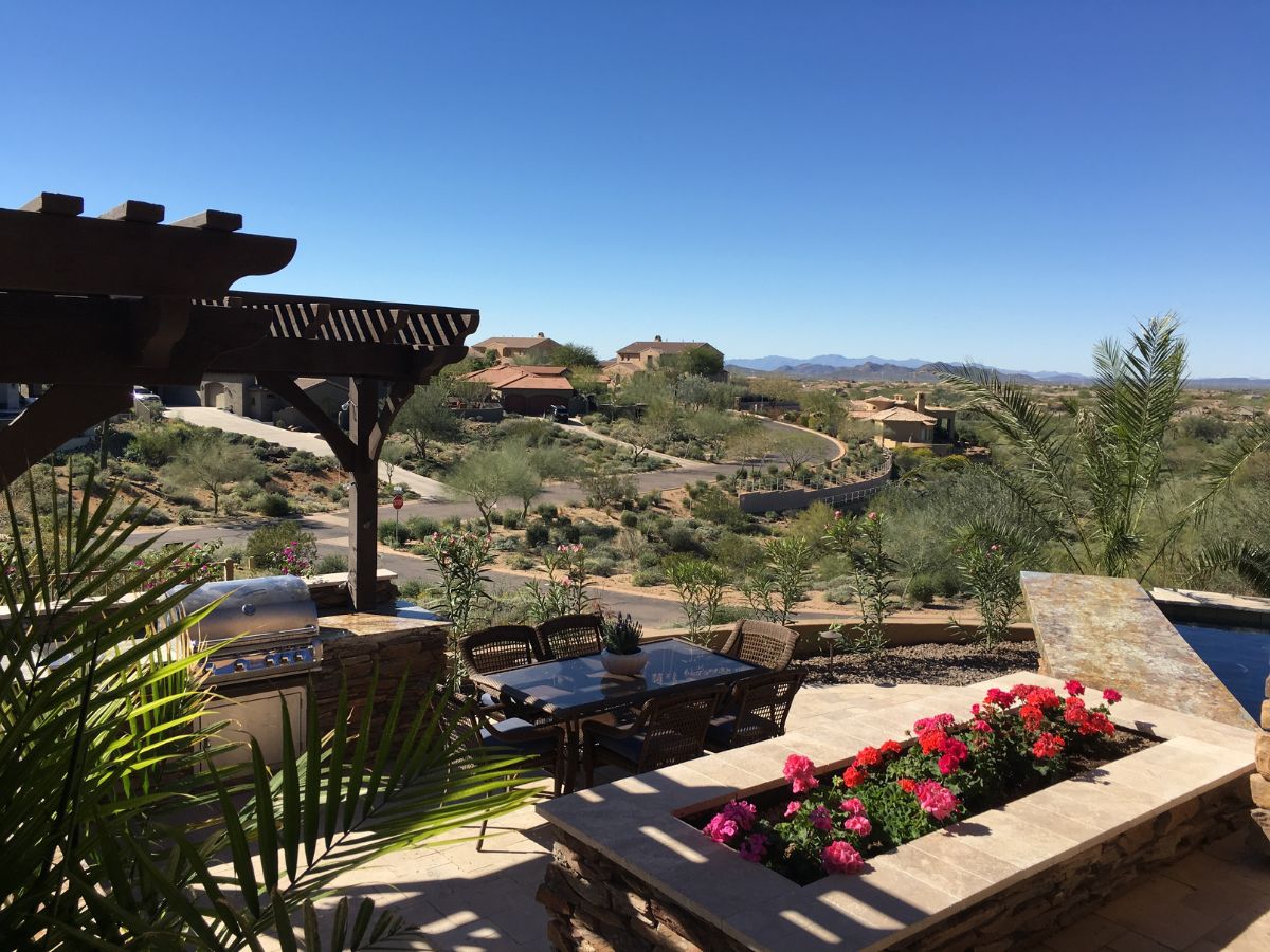 Sunny patio with pergola, outdoor dining, grill and flower planters overlooking desert homes and distant mountains
