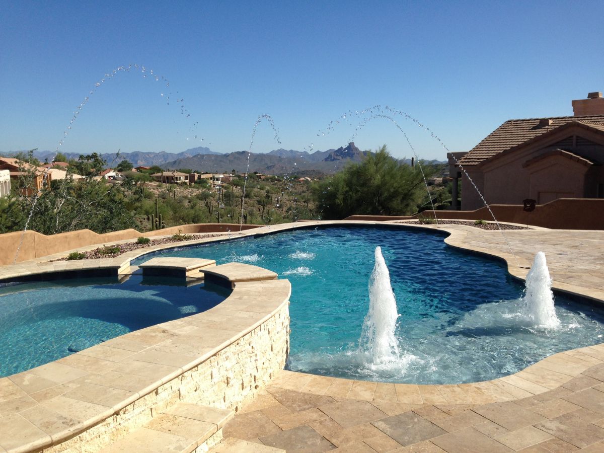 Luxury backyard swimming pool with spa, water jets and fountains overlooking desert landscape and distant mountains.
